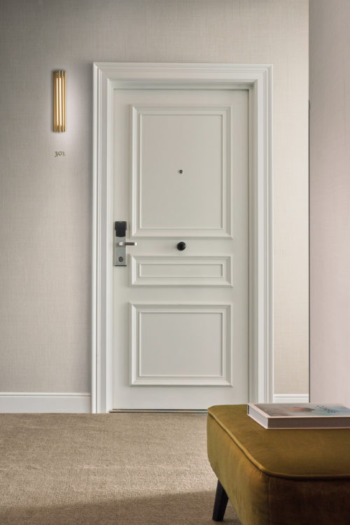 Omexco's High Performance Essence wallpaper in soft beige, paired with white accents and subtle lighting for a clean, elegant look.