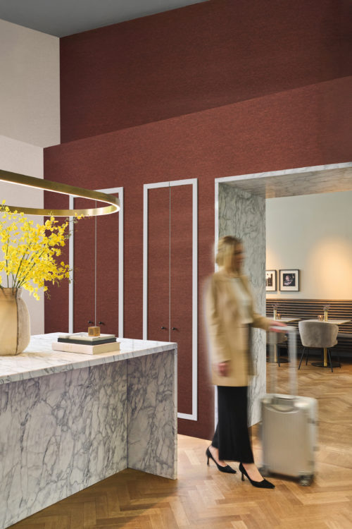 Omexco's High Performance Essence wallpaper in a deep textured red, adding warmth and contrast to a lobby space with marble surfaces, golden accents, and contemporary furnishings.