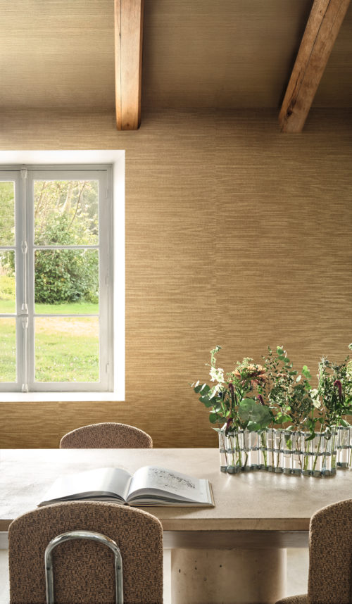 Omexco's Virginia's Garden wallpaper unfolds in golden warmth, where rustic beams and soft daylight frame a dining space rooted in nature.