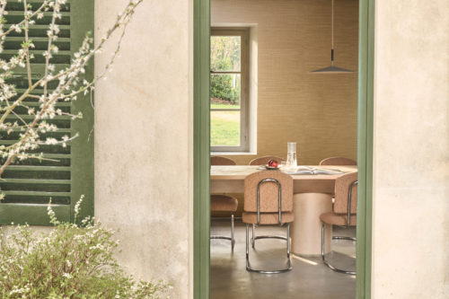 Omexco's Virginia's Garden wallpaper unfolds in golden warmth, where rustic beams and soft daylight frame a dining space rooted in nature.