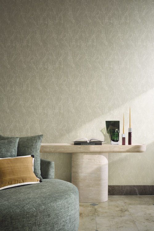 Raumgestaltung mit der Whisper Wandbekleidung von Omexco, die ein stilisiertes Motiv zeigt, inspiriert von feinen mineralischen Strukturen und Muscheln. Die hellgrüne strukturierte Wand dient als eleganter Hintergrund für einen grünen Sessel, einen Steinkonsolentisch und eine dunkelgrüne Glasvase.