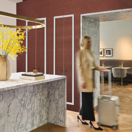 Omexco's High Performance Essence wallpaper in a deep textured red, adding warmth and contrast to a lobby space with marble surfaces, golden accents, and contemporary furnishings.