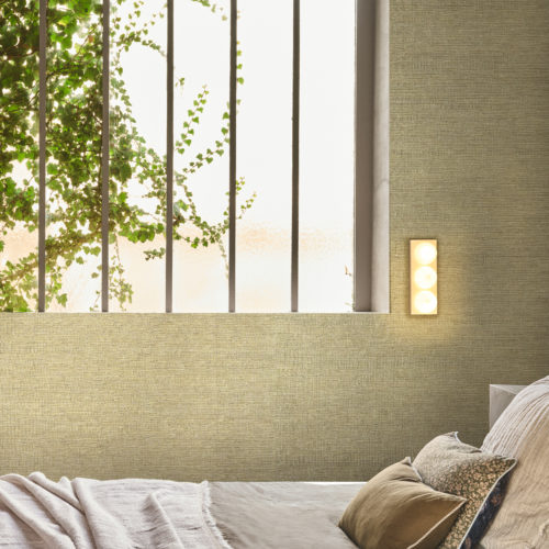 In the Virginia’s Garden collection, Omexco highlights the quiet elegance of textured wallpaper in a muted green tone, where subtle depth and organic weave bring a sense of nature indoors. Framed by soft light filtering through leafy vines at the window, the bedroom becomes a sanctuary of calm, its layered textiles and simple lines echoing the serenity of the outdoors. The design balances refinement and comfort, offering a timeless retreat that feels both modern and rooted in the natural world.