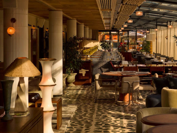 Stylish restaurant interior at Soho House Manchester featuring Omexco wallpaper in warm neutral tones, paired with patterned flooring, wooden ceilings and layered lighting. The Omexco wallpaper enhances the inviting atmosphere and complements the rich textures of the space.