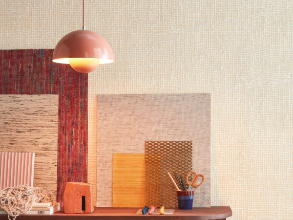 Interior designer's or architect’s inviting home office with a massive wooden shelving unit and pink vintage Flowerpot VP1 Hanging Lamp. We see samples of Omexco wallcoverings and other materials, books and small storage boxes laying on and in the shelving unit. On the wall, Omexco’s textile wallcovering collection “Loom Stories” is installed: a very textured weave of thick, off white yarns. A soothing neutral wall you would love to touch.