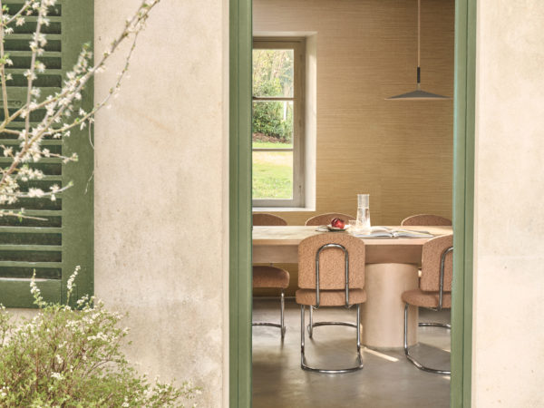 Omexco's Virginia's Garden wallpaper unfolds in golden warmth, where rustic beams and soft daylight frame a dining space rooted in nature.
